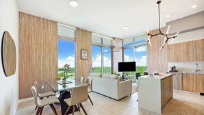 A modern living room with a glass dining table, a sofa, and a kitchen area with a TV. - 2 Bedroom -City View- Miami Design District - 1200 (Miami)