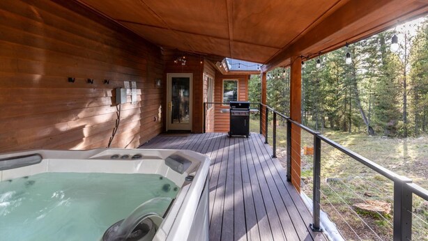 Eine Holzterrasse mit Whirlpool, Grill und einer Tür zu einem Innenbereich.