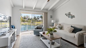 A modern living room with a large window overlooking a pool, a ceiling fan, and a sofa with decorative pillows.