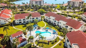A resort with multiple buildings, a central swimming pool, and a marina in the background.