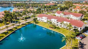 A resort with a large pool, white buildings with red roofs, and palm trees.