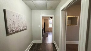 Un corridoio con pavimento in legno, una porta a destra e un'opera d'arte appesa al muro a sinistra.
