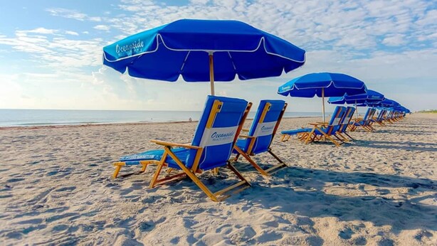 Strandstühle und Sonnenschirme an einem sandigen Strand mit Blick auf das Meer.