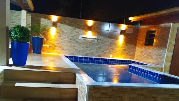 Una piscina exterior con diseño de piedra y azulejos, rodeada por un muro de piedra y un conjunto de escalones de madera que conducen a ella.