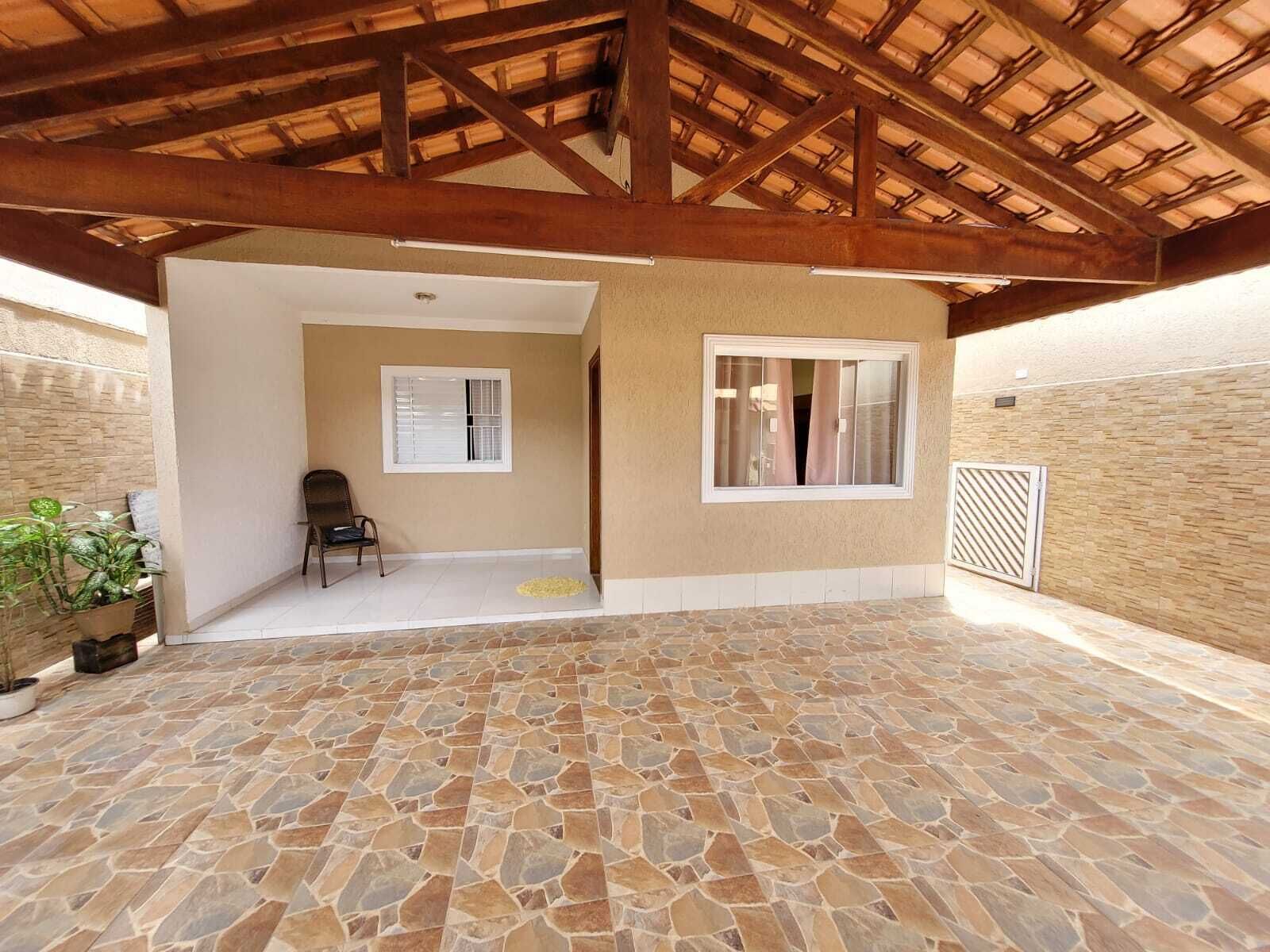 A covered patio with stone flooring, wooden beams, and a view of an interior room with a chair and a window.