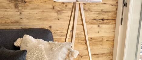 A room with a dark grey sofa, a white lamp on a wooden tripod stand, and a wooden wall.