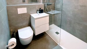 Moderni kylpyhuone, jossa on lasiseinällä varustettu suihku, valkoinen pesuallas peilillä sekä wc-istuin.