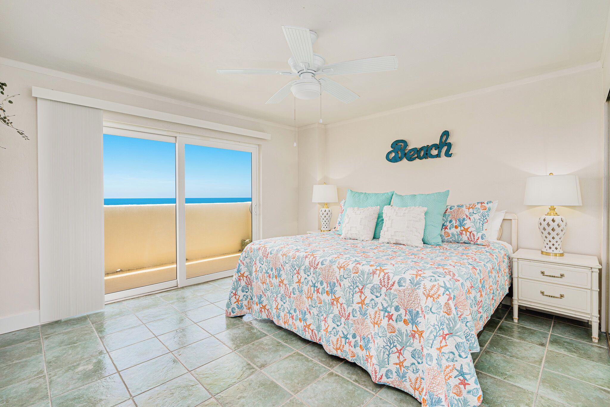 Une chambre avec un lit, des tables de chevet, un ventilateur de plafond et une vue sur la plage.