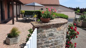 Une cour avec un mur en pierre, un pot de fleurs orné de fleurs roses et un bâtiment doté d’un toit en tuiles.