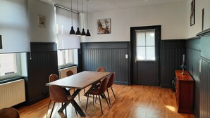 Un coin repas avec une table et des chaises en bois, une porte noire et une fenêtre avec des stores.