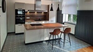 Une cuisine moderne dotée d’un îlot central, de deux suspensions et d’une fenêtre donnant sur un paysage verdoyant.