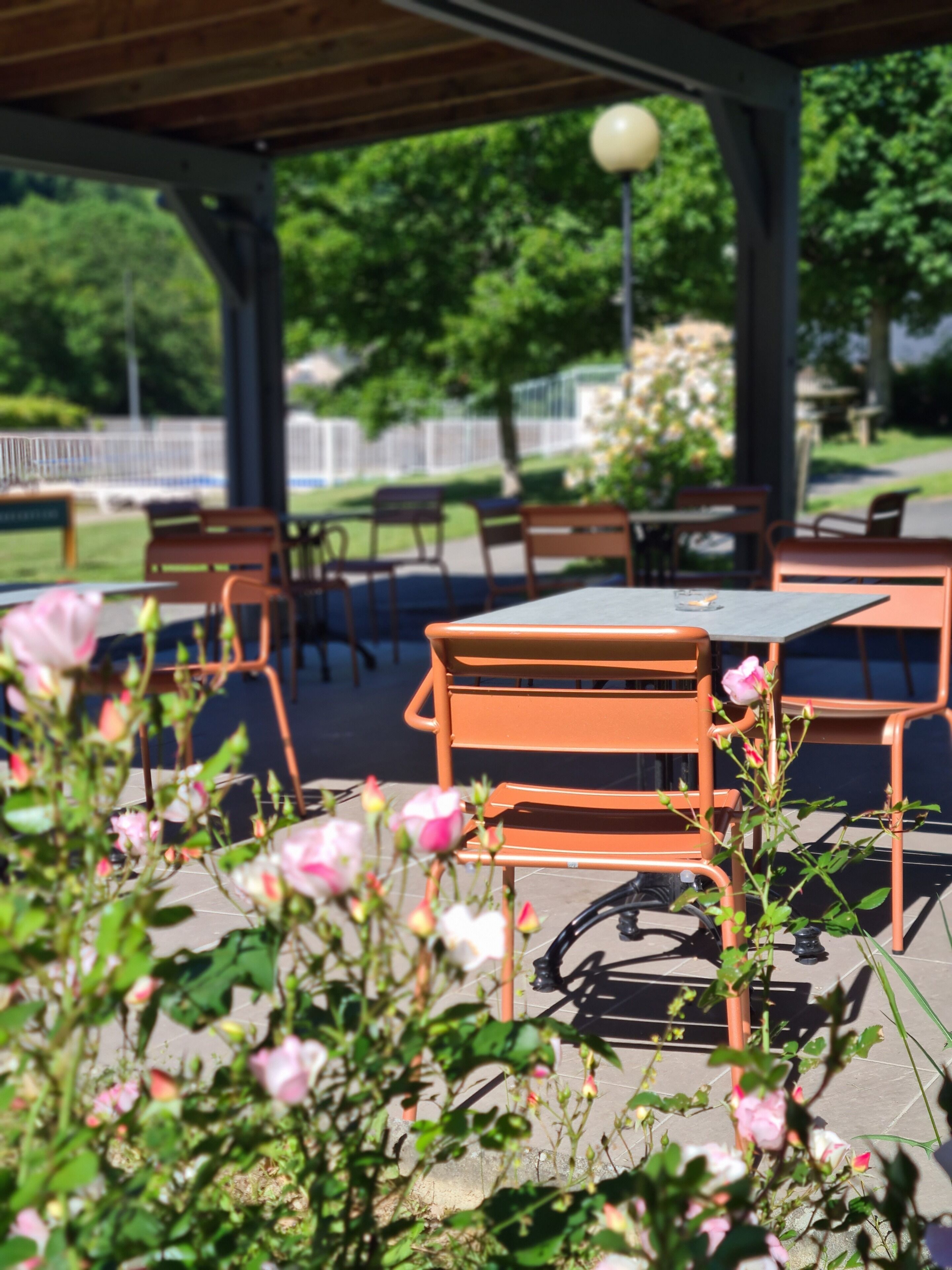 An outdoor patio area with wooden tables and chairs, surrounded by greenery and flowers.