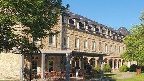 A stone building with a covered patio and outdoor seating area. - LOGIS HOTEL - L'HÔTEL DES BAINS (Salles-la-Source)