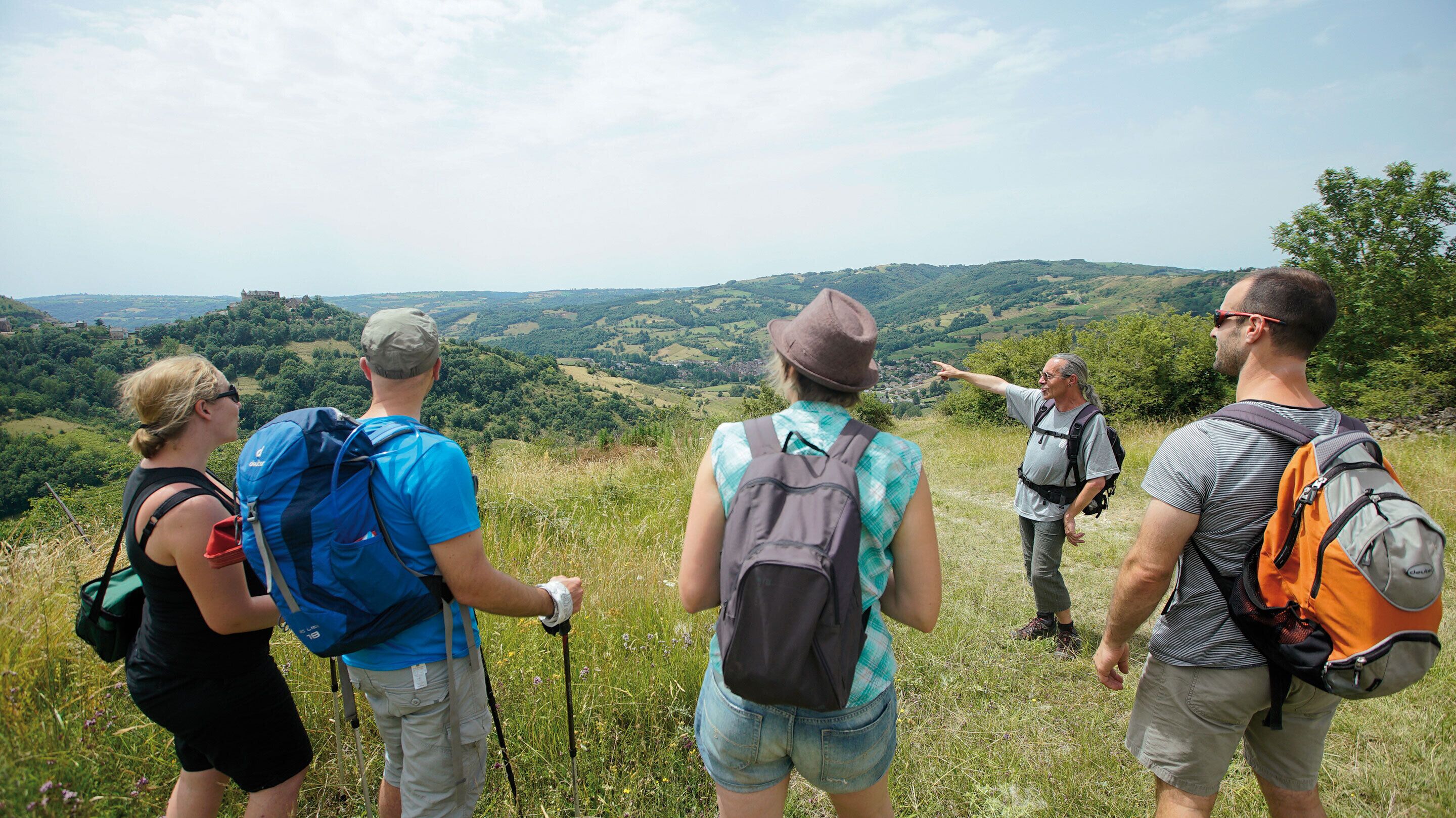 Un groupe de randonneurs se trouve sur une colline herbeuse, d’où l’on peut admirer des collines verdoyantes à l’horizon.