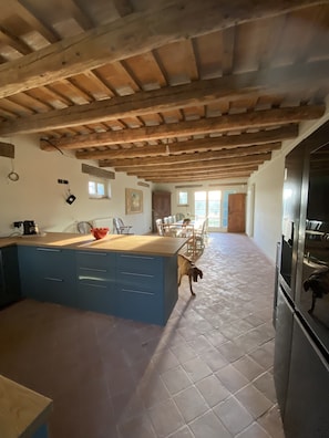 A spacious kitchen with a large island, wooden beams on the ceiling, and a tiled floor.