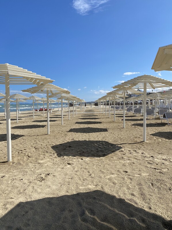 A beach with white umbrellas and chairs, a boat in the water, and a clear sky.