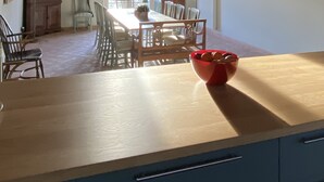 Ein Essbereich mit Holztisch und Stühlen, eine rote Schüssel auf dem Tisch und Blick ins Freie durch große Fenster.