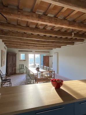A dining area with a wooden table and chairs, a red bowl on the table, and a view of the outdoors through large windows.
