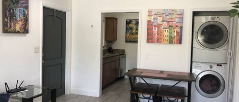 A compact living space with a dining table, two chairs, a washing machine, and artwork on the walls.