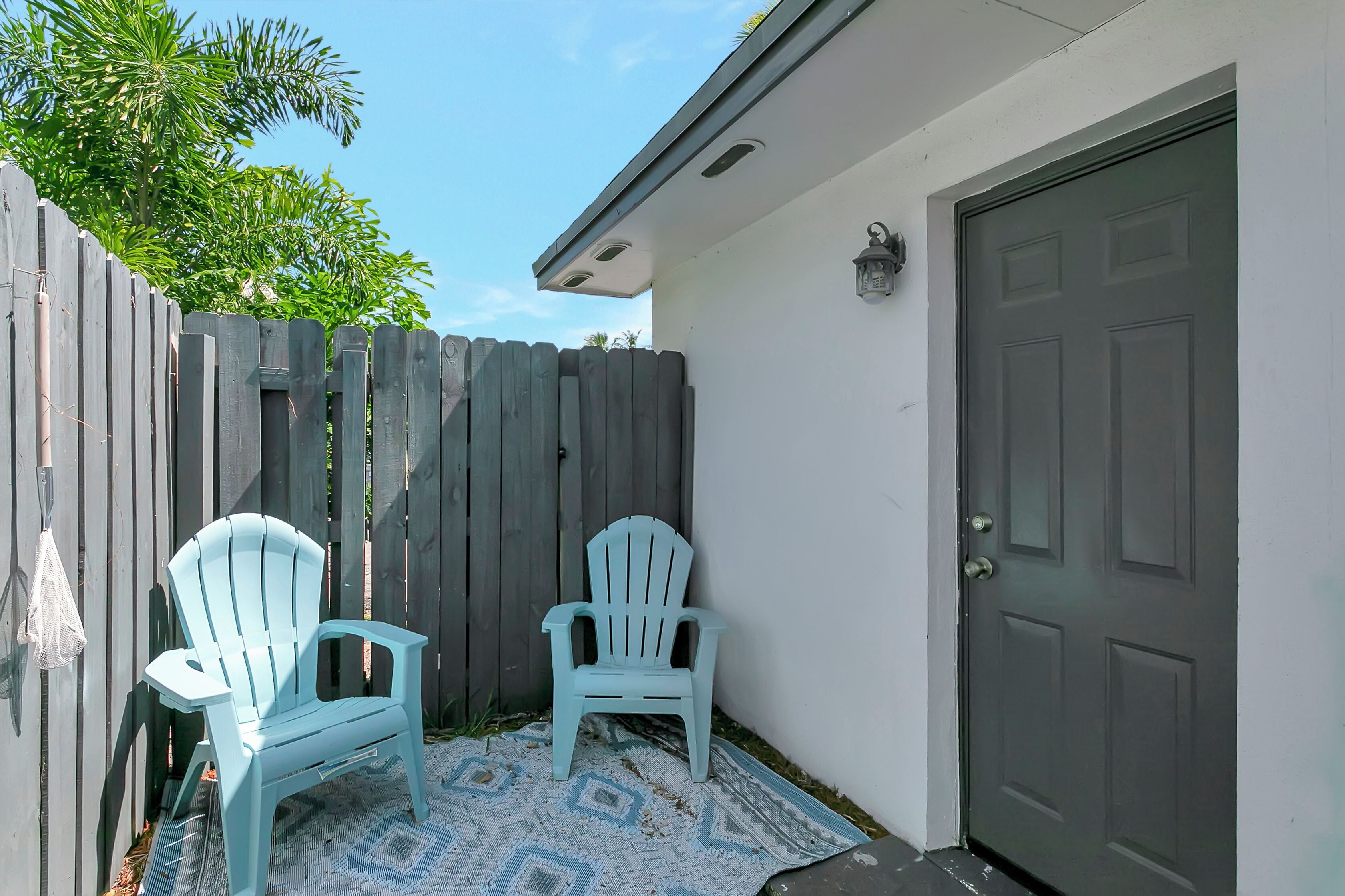 A patio area with two light blue Adirondack chairs, a patterned rug, and a wooden fence.