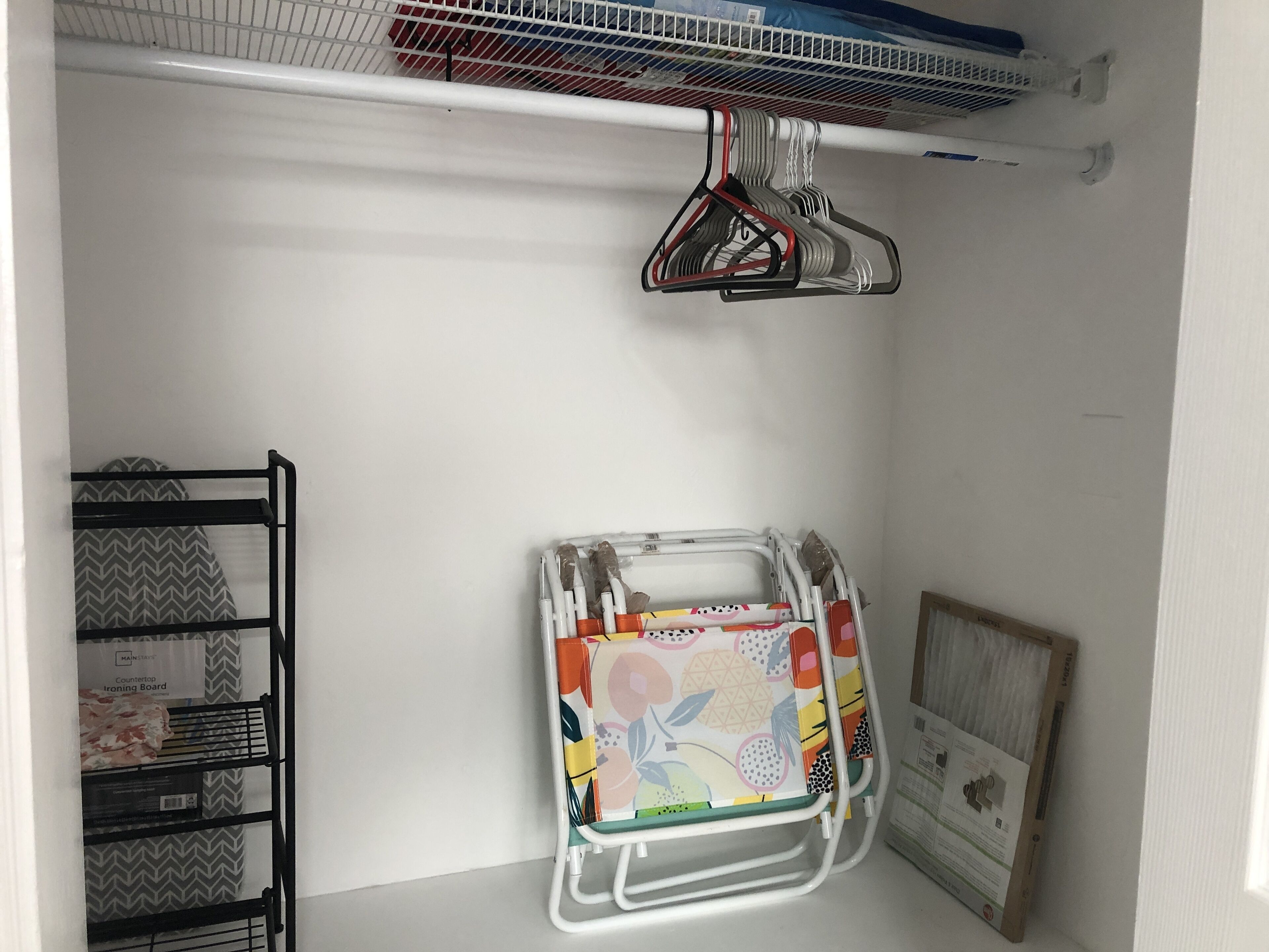 Un coin de pièce avec un mur blanc, une étagère en métal recouverte d’un tissu à motifs et une planche à repasser colorée.