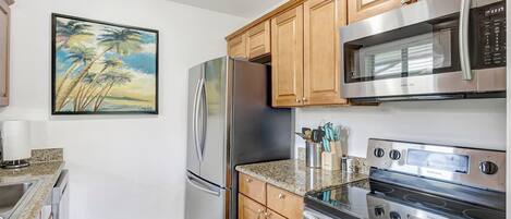 A modern kitchen with stainless steel appliances, wooden cabinets, and a granite countertop.
