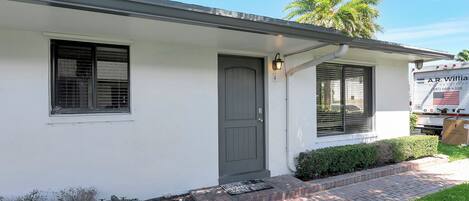 A single-story house with a grey door, a small window with blinds, and a mailbox.
