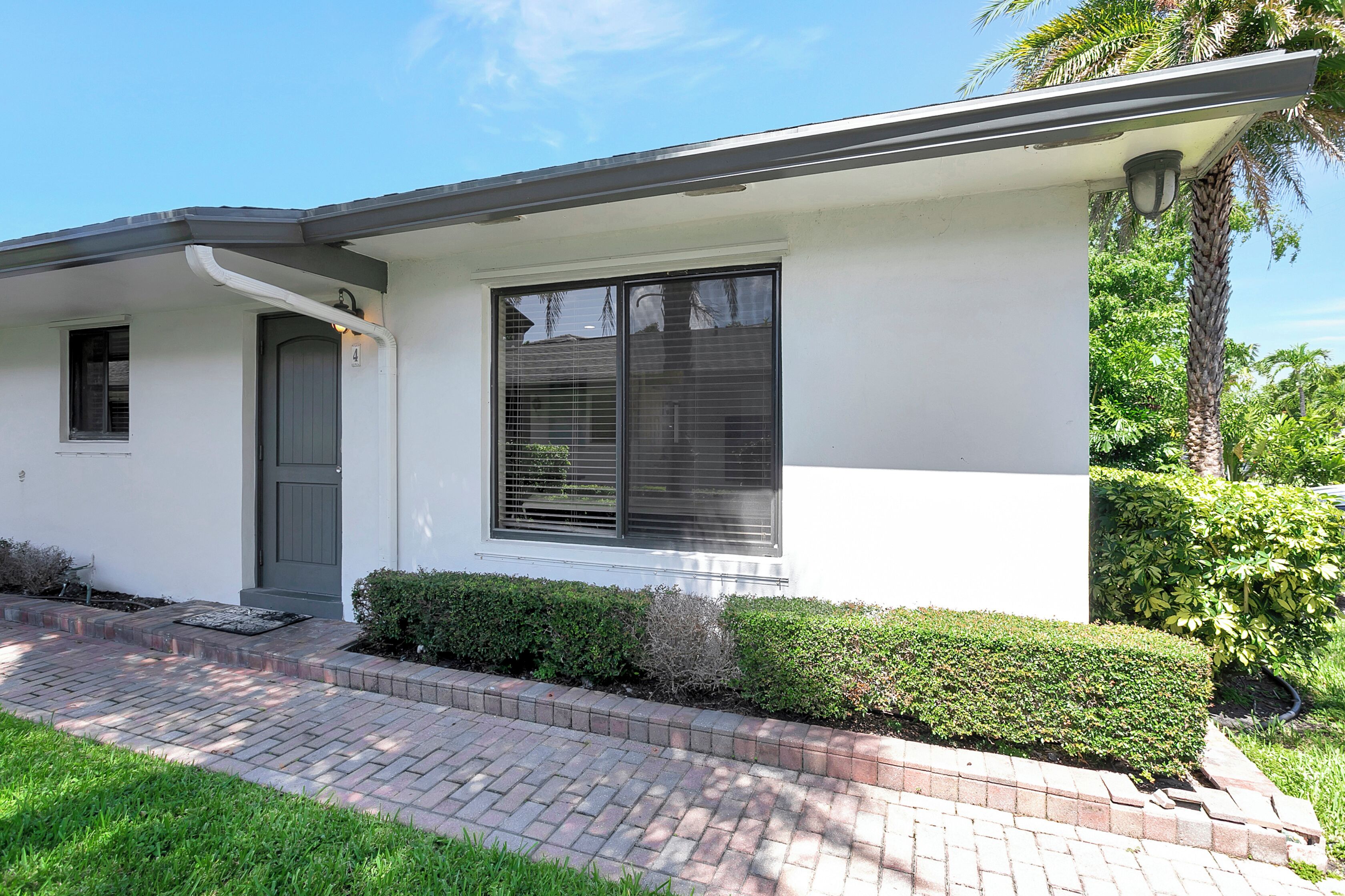 A modern house with a grey door, a large window with blinds, and a brick pathway leading to the entrance.
