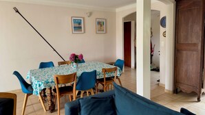 A dining area with a table set for four, blue chairs, and a vase with flowers. There are two framed pictures on the wall.
