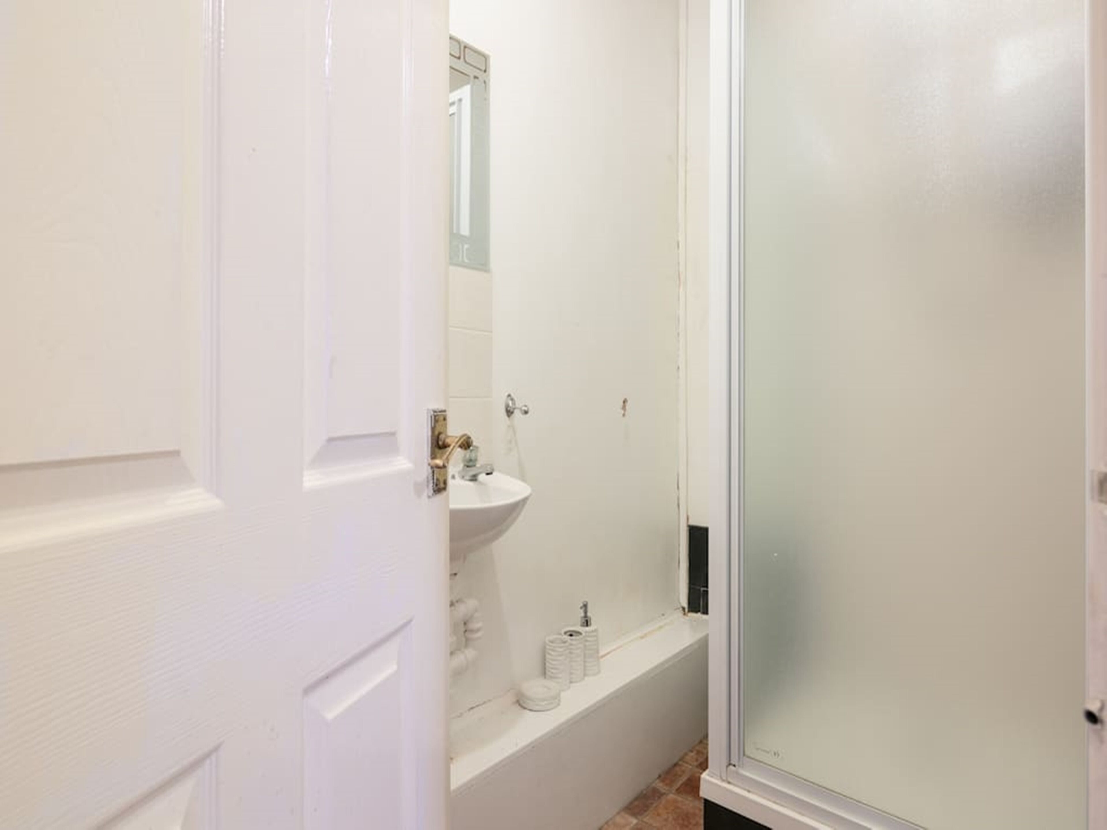 Un baño con lavamanos blanco, espejo y cabina de ducha de vidrio.