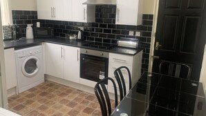 A compact kitchen with a washing machine, oven, and a black tiled backsplash. - Short Term Shared R&R In Chorlton (Manchester)