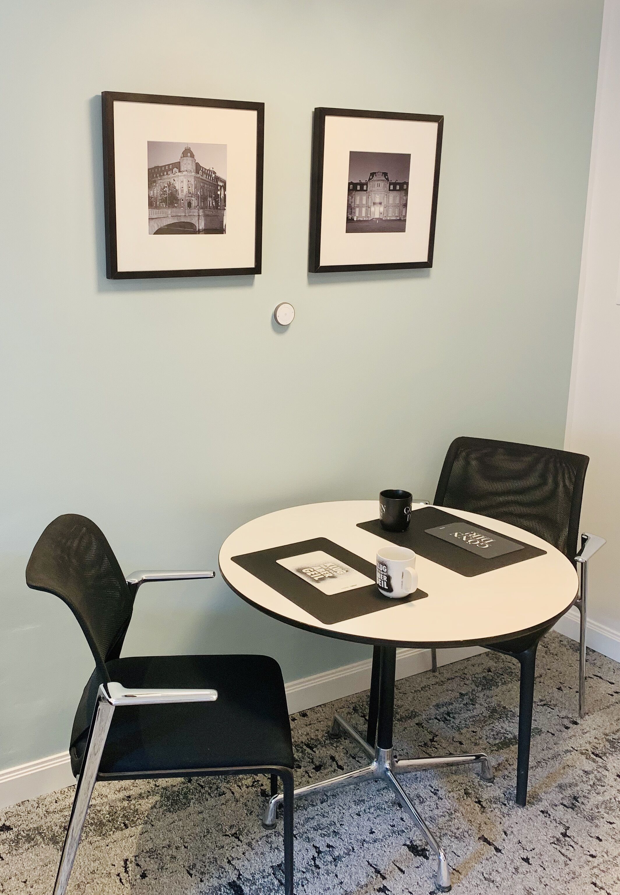 A conference room with a round table, two chairs, framed pictures on the wall, and a coffee mug on the table.