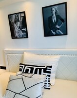 A bedroom with a white bed, multiple pillows, and two framed pictures on the wall.