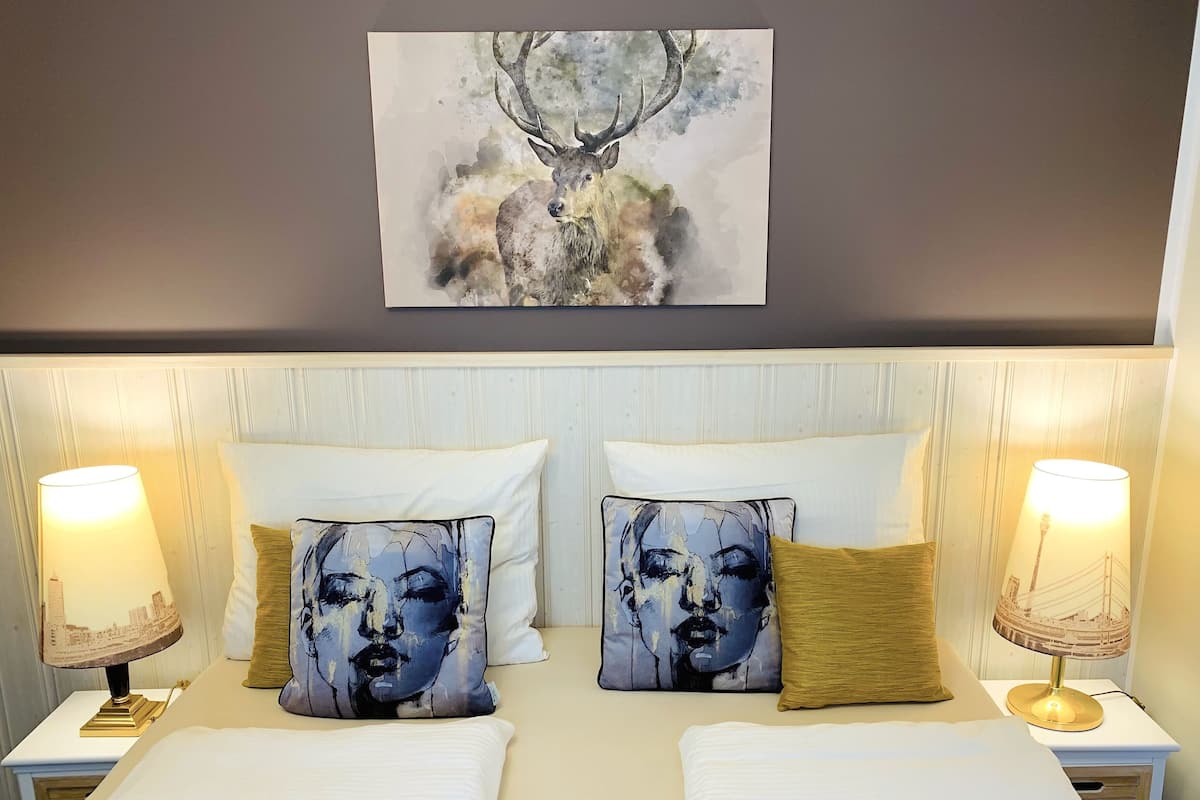 A hotel room with a large painting of a deer above the bed, two bedside lamps, and two pillows with abstract designs.
