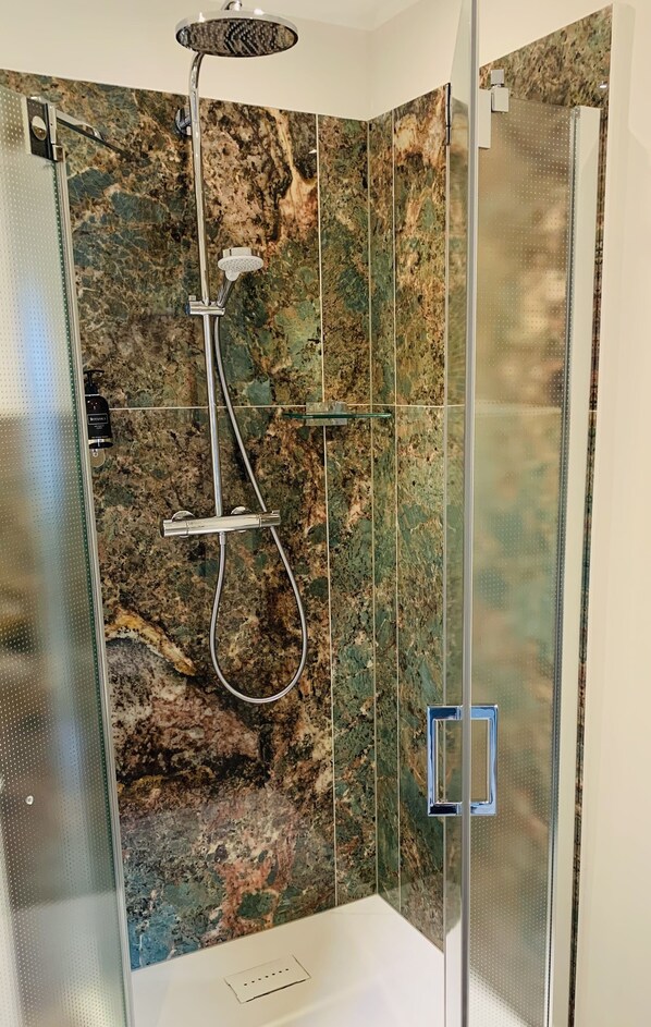 Une salle de bain moderne dotée d’une douche à parois de verre, d’un pommeau de douche amovible et d’un robinet amovible.