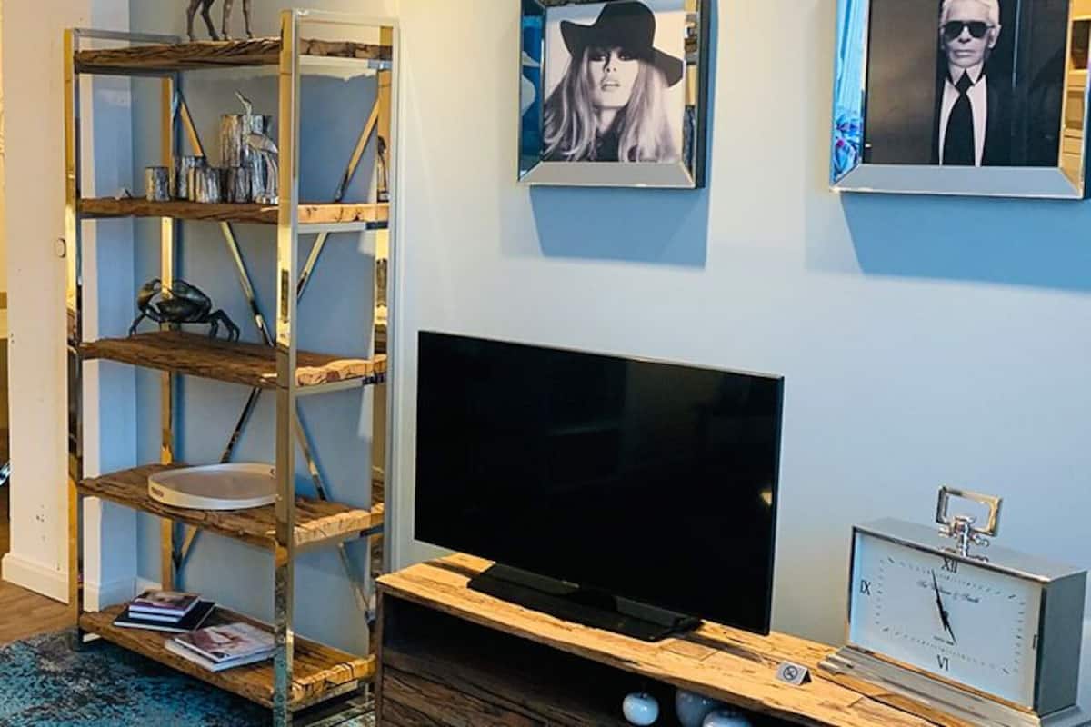 A living room with a TV, wooden shelves, a dining area, and a kitchen visible in the background.