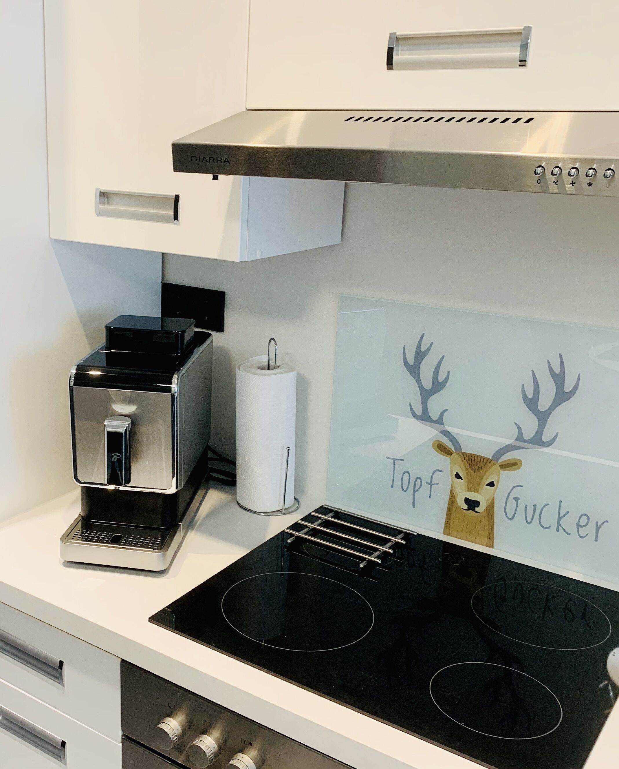 Eine Küche mit Kaffeemaschine, Papierhandtuchhalter und einem Schild mit einer Hirsch-Illustration und dem Text "Topf Gucker".