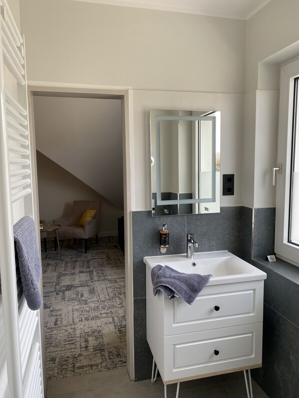 Un baño moderno con un lavabo blanco, paredes de azulejos oscuros y un espejo arriba.