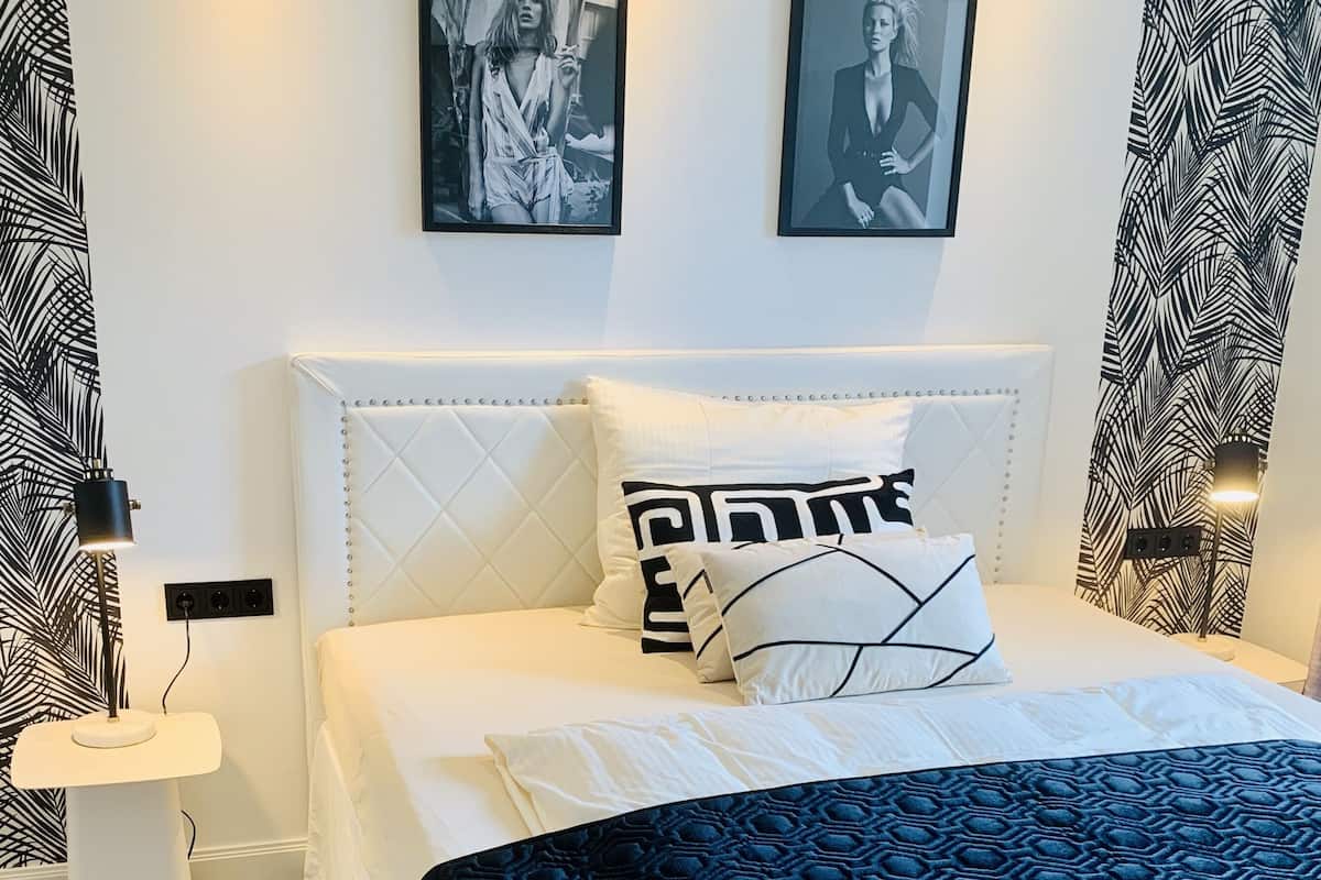 A neatly arranged bedroom with a bed, pillows, a nightstand, and wall art.