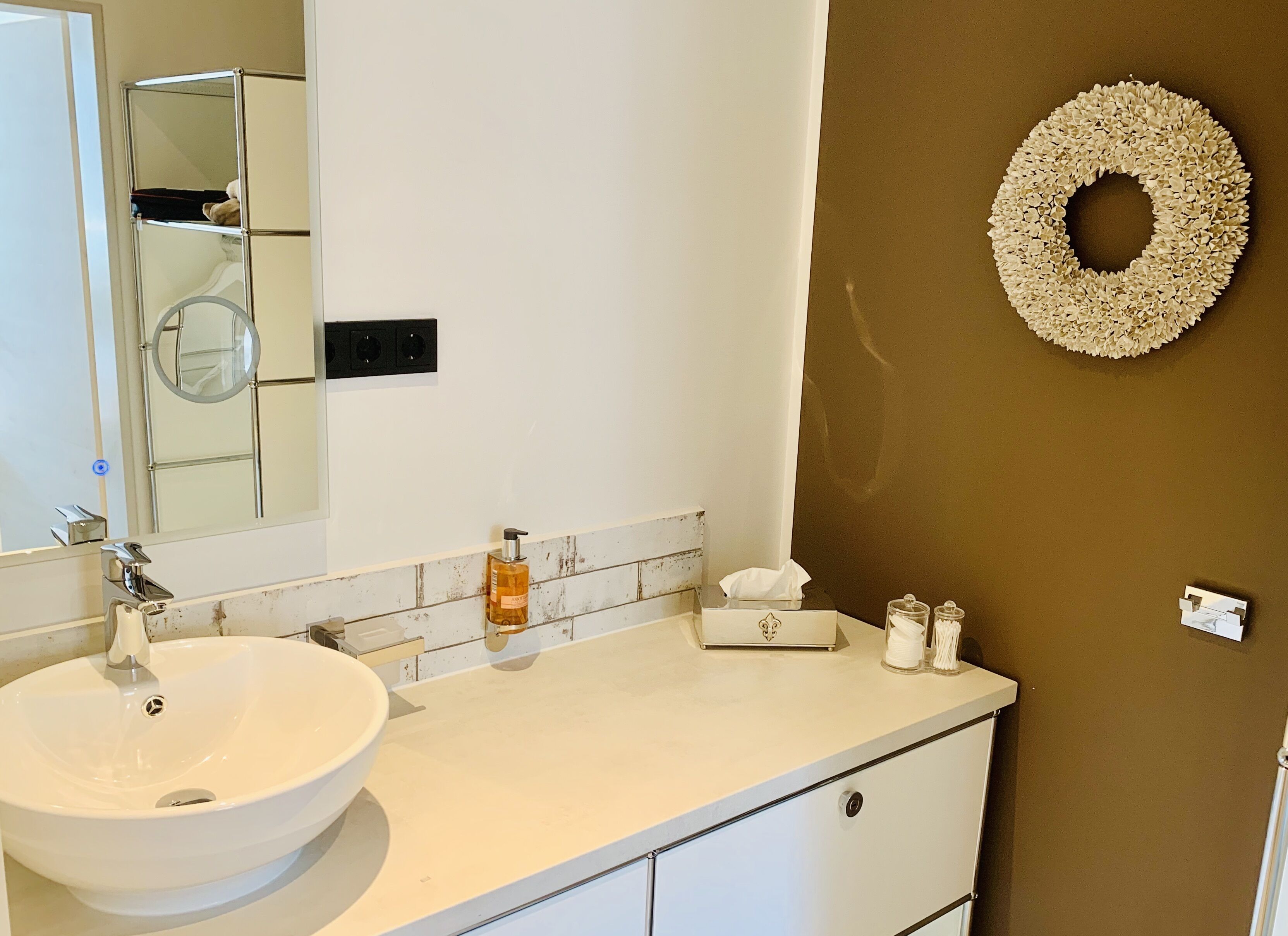 A bathroom with a white sink, a mirror, a towel dispenser, and a decorative wreath on the wall.