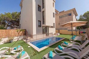 A modern two-story building with a swimming pool, outdoor seating, and a well-maintained lawn.