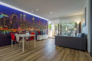 A modern living room with a cityscape mural, a dining area with red chairs, and a grey sofa.