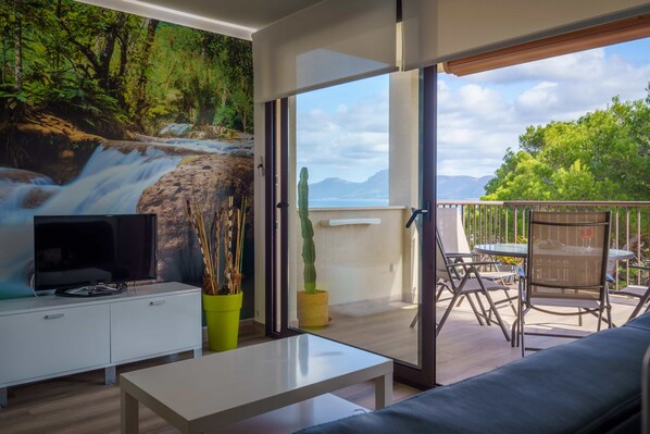 A modern living room with a TV, a sofa, and a dining area with outdoor seating.