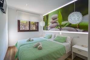 A bedroom with a bed, pillows, a nightstand, a window, and a wall-mounted light fixture.