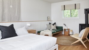 Un dormitorio con cama, un sofá verde, una silla, una mesita de noche, una lámpara, una ventana con cortinas y una chimenea.
