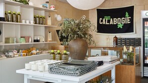 Un espacio comercial limpio y moderno con estanterías blancas, una mesa central con un jarrón grande y un letrero que dice "CALABOGIE".