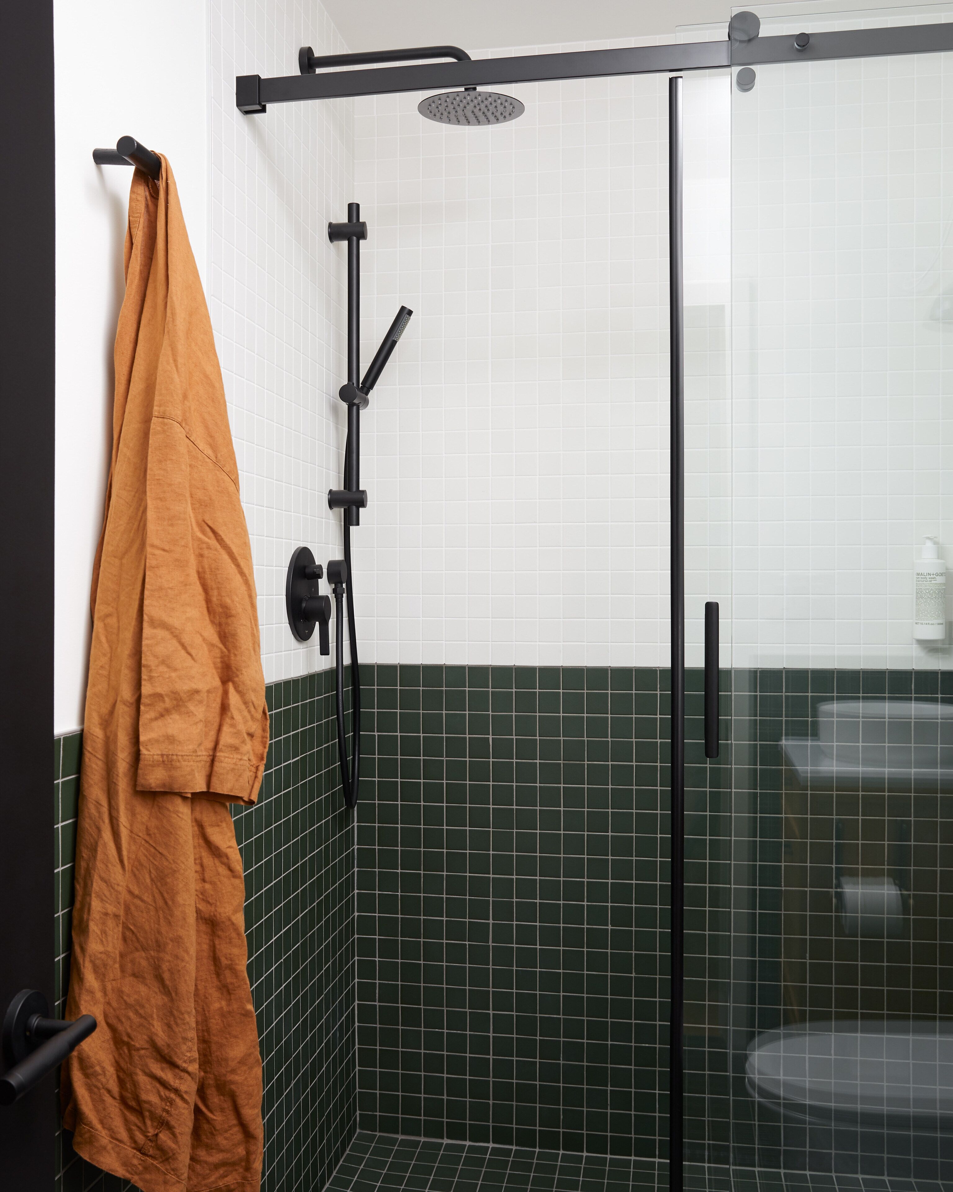 Un baño moderno con cabina de ducha de vidrio, paredes de azulejos blancos y detalles en azulejos verdes tipo metro.
