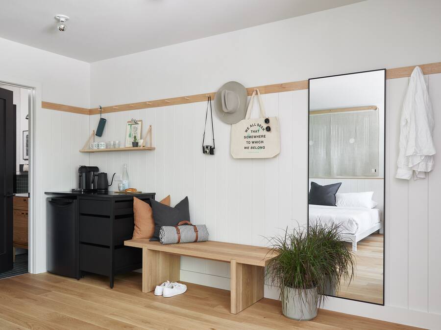 Une chambre à coucher moderne avec un banc en bois, un miroir, une table de chevet avec un appareil photo et une plante en pot.