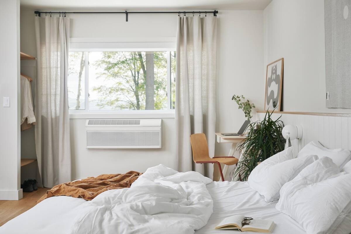 Une chambre à coucher comprenant un lit, une chaise, un bureau, une fenêtre et un climatiseur.