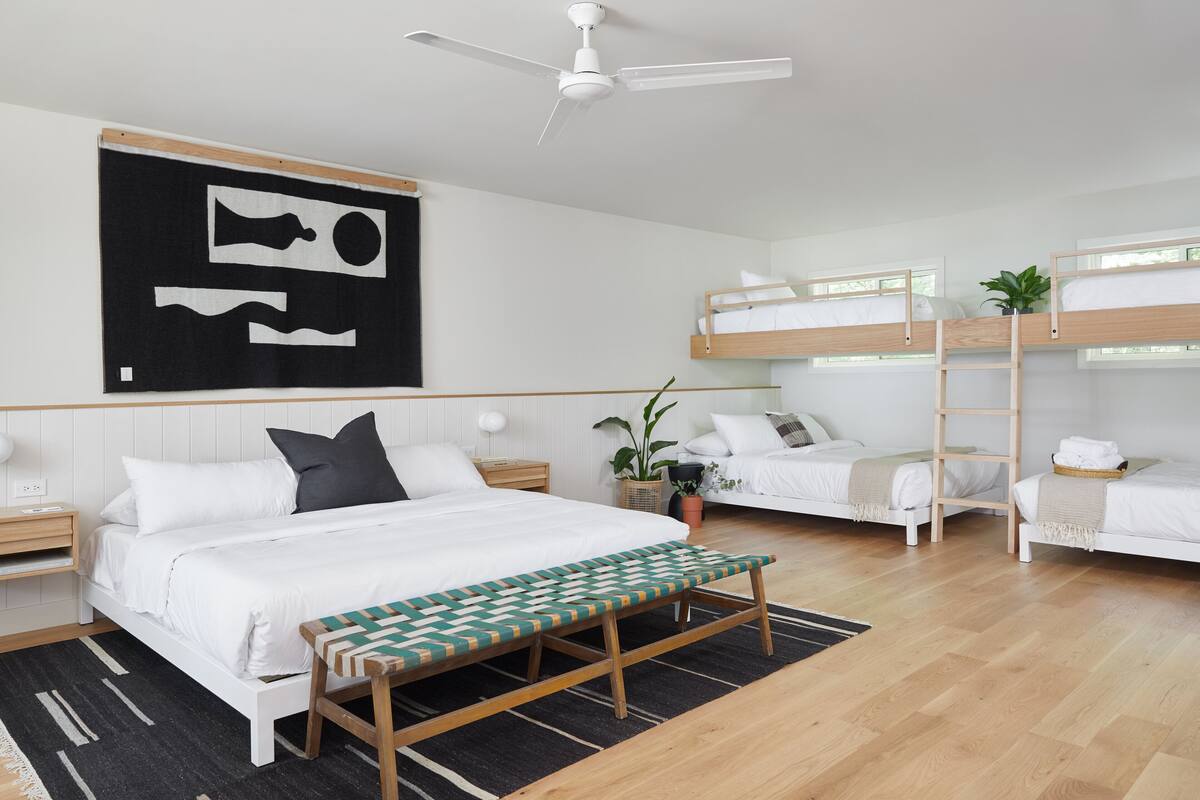 Une chambre d’hôtel moderne dotée d’un grand lit, d’une banquette, de deux lits superposés, d’un ventilateur de plafond et d’une œuvre d’art accrochée au mur.